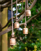 Gold bells hanging from ropes against a natural background with greenery