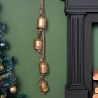 Decorative gold bell hanging on a green wall next to a Christmas tree and fireplace.